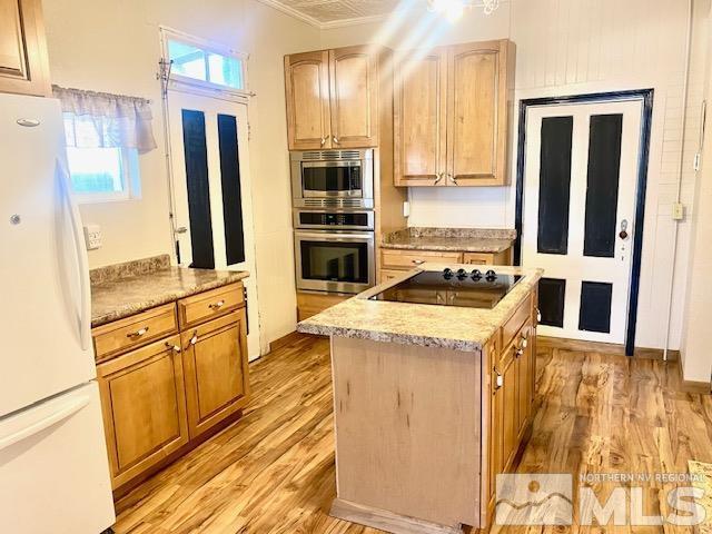 85 S Main, Paradise Valley, NV 89426 - kitchen featuring appliances with stainless steel finishes, light wood-type flooring, a kitchen island, ornamental molding, and light stone counters