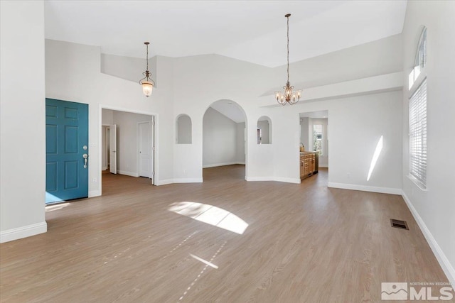unfurnished living room featuring wood finished floors, high vaulted ceiling, a chandelier, arched walkways, and baseboards