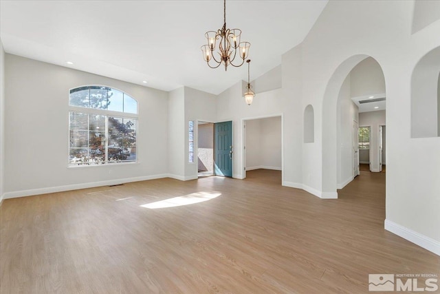 spare room featuring healthy amount of natural light, light wood finished floors, a chandelier, baseboards, and high vaulted ceiling