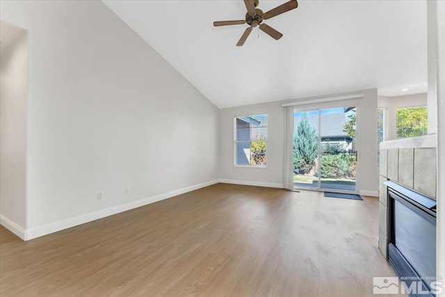 unfurnished living room featuring baseboards, ceiling fan, wood finished floors, a tiled fireplace, and high vaulted ceiling