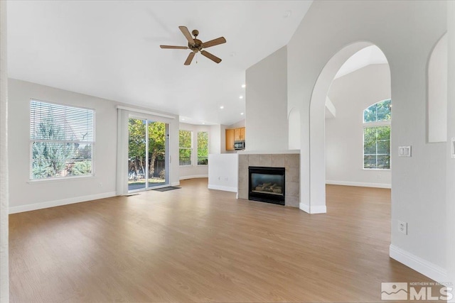 unfurnished living room featuring ceiling fan, a tiled fireplace, light wood-style flooring, baseboards, and high vaulted ceiling