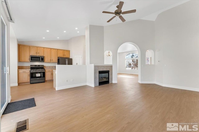 unfurnished living room featuring ceiling fan, high vaulted ceiling, light wood-type flooring, a tiled fireplace, and baseboards