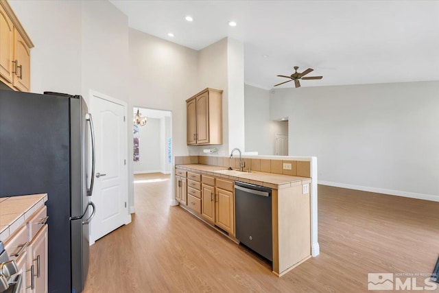 kitchen featuring appliances with stainless steel finishes, tile counters, a ceiling fan, a peninsula, and a sink