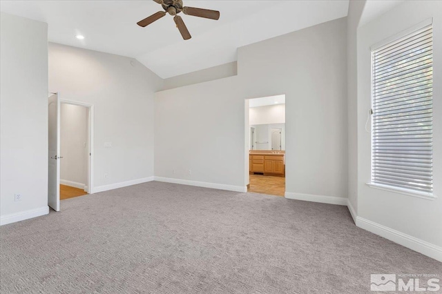 unfurnished bedroom with vaulted ceiling, light carpet, baseboards, connected bathroom, and ceiling fan