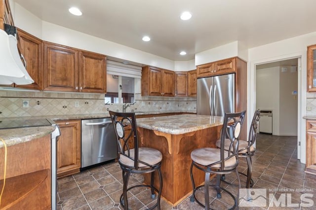 kitchen with appliances with stainless steel finishes, a center island, a breakfast bar, brown cabinets, and decorative backsplash