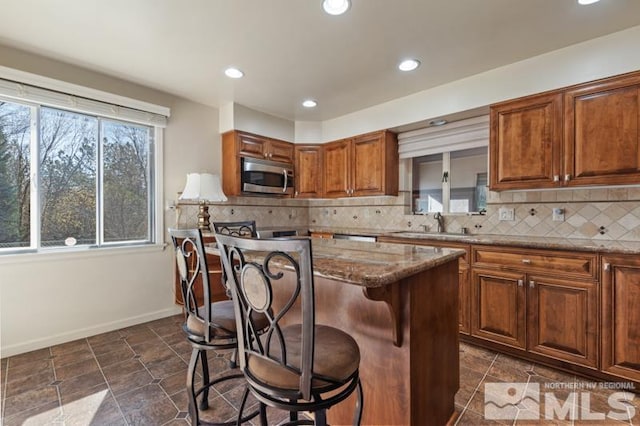kitchen with stainless steel microwave, a kitchen island, a breakfast bar, backsplash, and stone counters