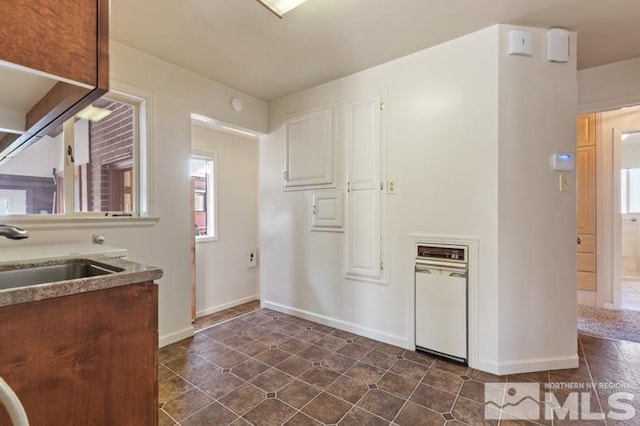 kitchen featuring a sink, plenty of natural light, baseboards, and dark tile patterned flooring
