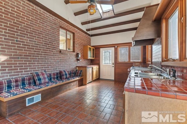 kitchen with tile counters, ceiling fan, premium range hood, a sink, and glass insert cabinets