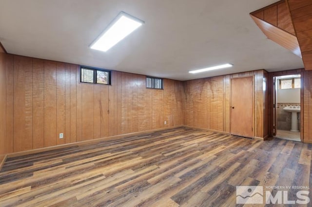 basement with wood finished floors, healthy amount of natural light, wood walls, and a sink