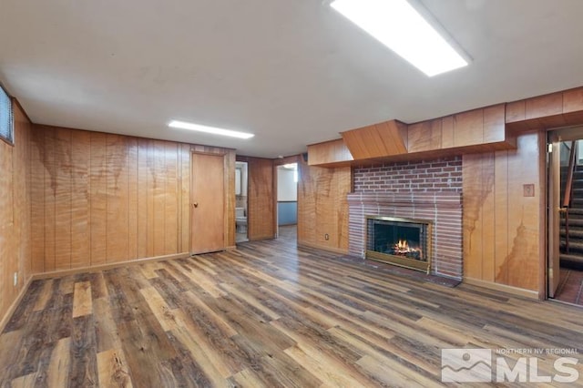 unfurnished living room with wood finished floors, wooden walls, a fireplace, and stairway