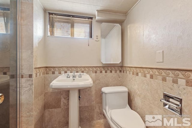 full bath featuring tile walls, toilet, a wainscoted wall, a shower, and a sink