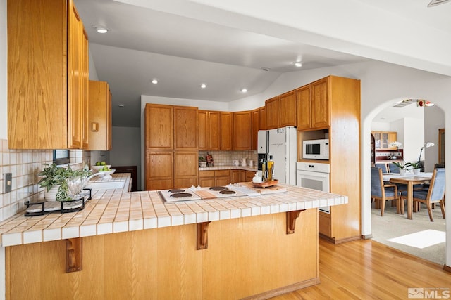 80 Cassas Ct, Reno, NV 89511 - kitchen with white appliances, a peninsula, light wood-style flooring, arched walkways, and backsplash