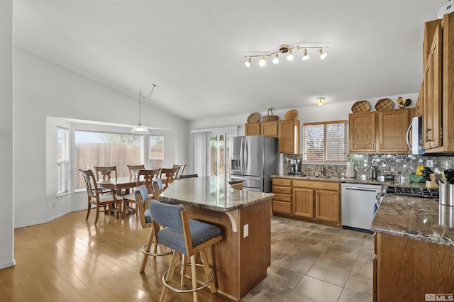 1018 Ringneck, Sparks, NV 89441 - kitchen featuring stainless steel appliances, brown cabinetry, vaulted ceiling, a breakfast bar area, and a kitchen island