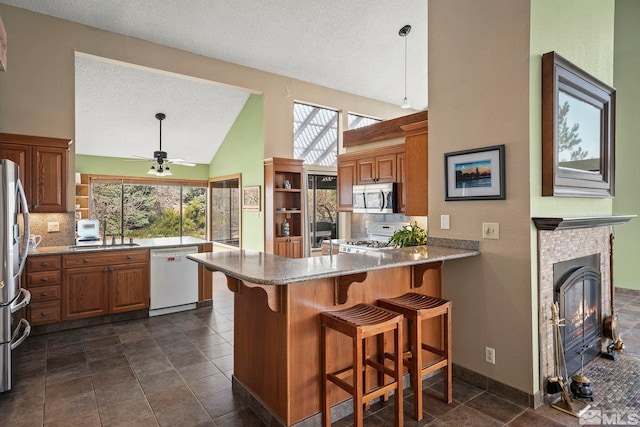 12880 Roseview Ln, Reno, NV 89511 - kitchen with appliances with stainless steel finishes, a peninsula, backsplash, brown cabinetry, and a textured ceiling