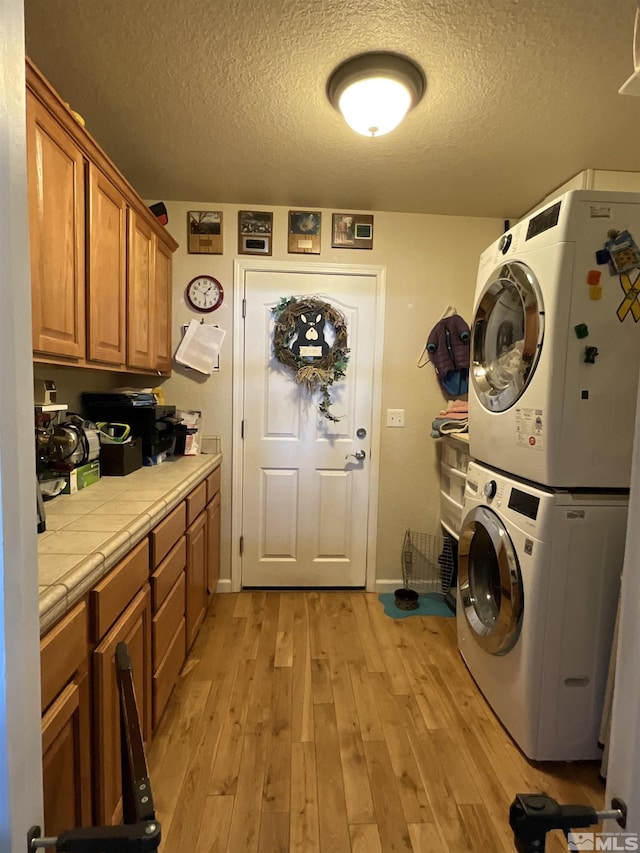 5710 Sarah Rd, Fallon, NV 89406 - laundry area featuring stacked washer and clothes dryer, a textured ceiling, light wood finished floors, baseboards, and cabinet space