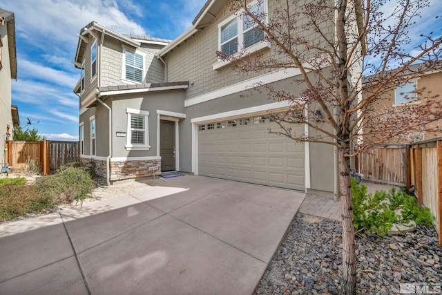 view of front of house with an attached garage, fence, stone siding, stucco siding, and concrete driveway