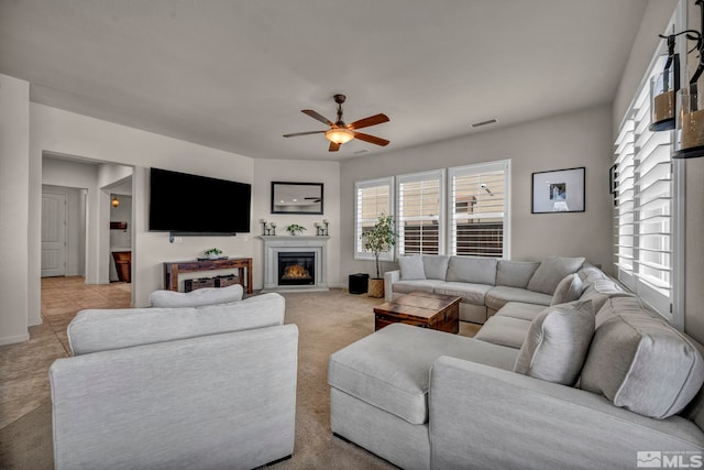 living area featuring a glass covered fireplace, ceiling fan, and light carpet