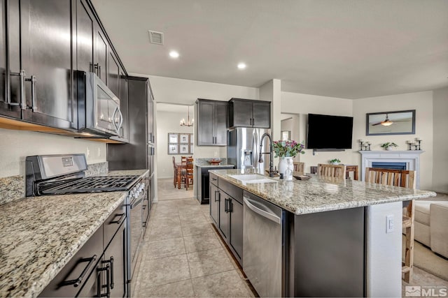 kitchen with stainless steel appliances, a sink, light stone countertops, a kitchen island with sink, and a breakfast bar
