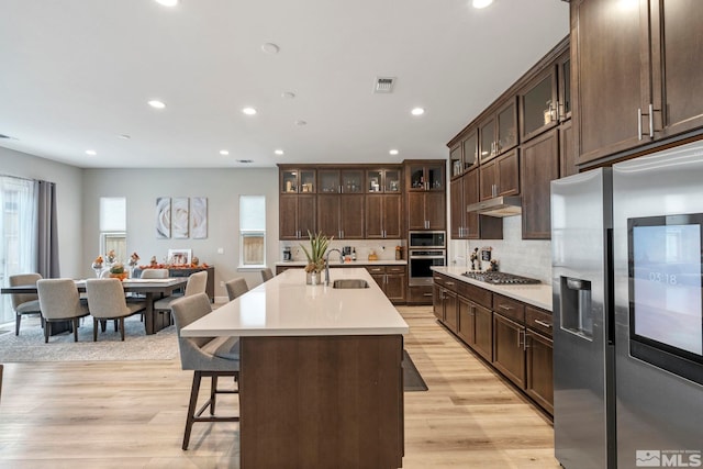kitchen with stainless steel appliances, a sink, light countertops, light wood finished floors, and a kitchen bar