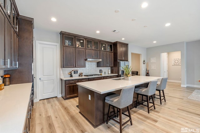 kitchen with stainless steel appliances, a breakfast bar, a sink, light wood-style floors, and a kitchen island with sink