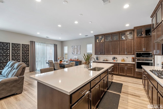 kitchen with stainless steel appliances, a sink, open floor plan, light countertops, and light wood-type flooring