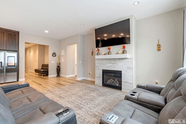 living room featuring light wood-style floors, a tile fireplace, recessed lighting, and baseboards