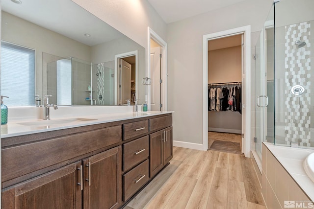 full bathroom featuring a stall shower, double vanity, wood finished floors, a walk in closet, and a bathtub