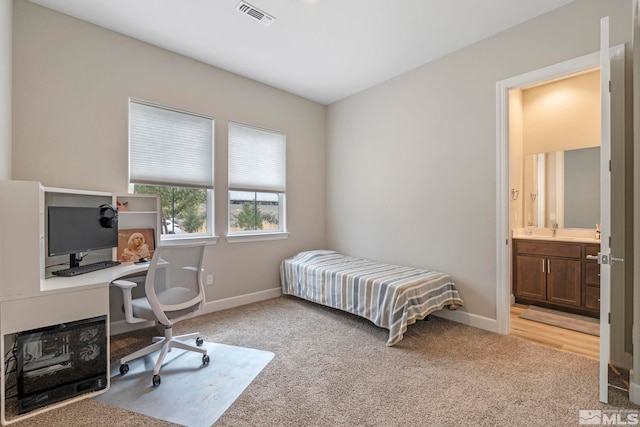 bedroom featuring light colored carpet, baseboards, a desk, a sink, and ensuite bathroom