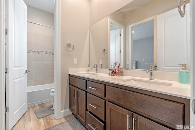 full bathroom featuring double vanity, toilet, wood finished floors, and washtub / shower combination