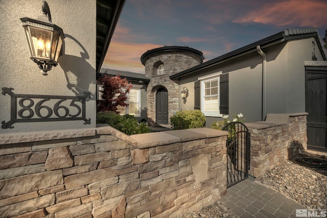 property entrance with stucco siding, stone siding, and a gate