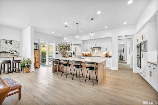 kitchen featuring built in appliances, under cabinet range hood, a kitchen breakfast bar, light wood-style floors, and recessed lighting
