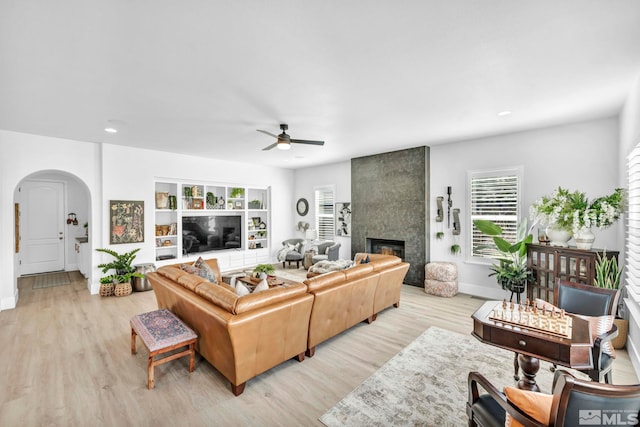 living area with a ceiling fan, arched walkways, a tile fireplace, wood finished floors, and baseboards
