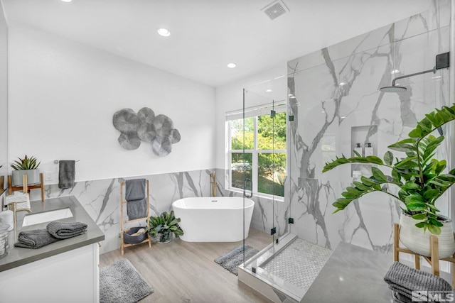 bathroom with a marble finish shower, a freestanding tub, wood finished floors, tile walls, and recessed lighting