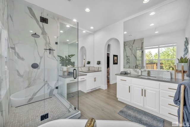 bathroom with a marble finish shower, recessed lighting, wood finished floors, and two vanities