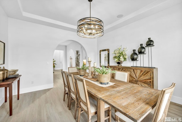 dining area featuring arched walkways, a chandelier, light wood finished floors, a tray ceiling, and baseboards
