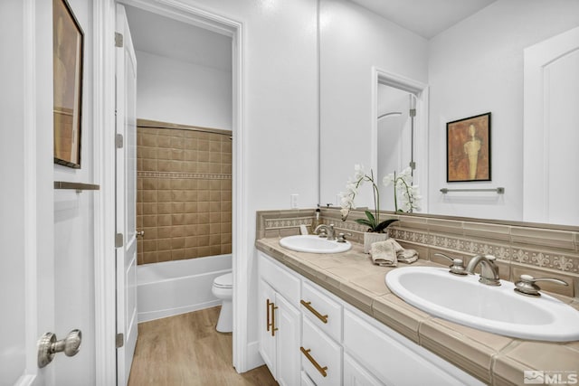 full bath featuring wood finished floors, double vanity, toilet, and tasteful backsplash