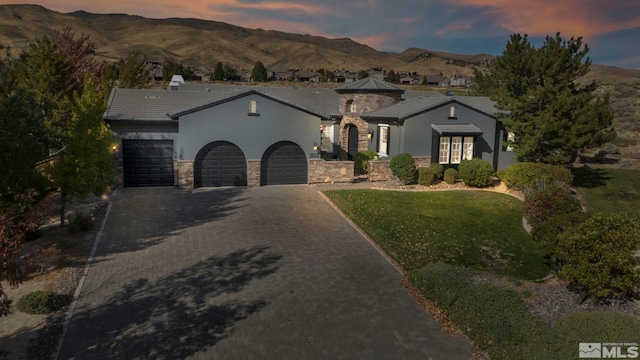 view of front of home with stucco siding, stone siding, a garage, decorative driveway, and a mountain view