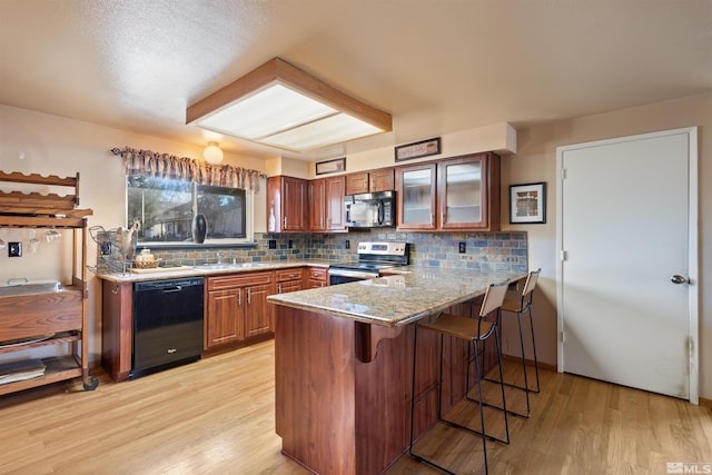 kitchen featuring stainless steel electric range, black dishwasher, a breakfast bar, light wood-style floors, and a peninsula