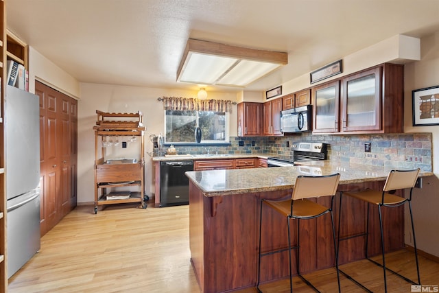 kitchen featuring appliances with stainless steel finishes, a peninsula, backsplash, light wood-style flooring, and light stone counters