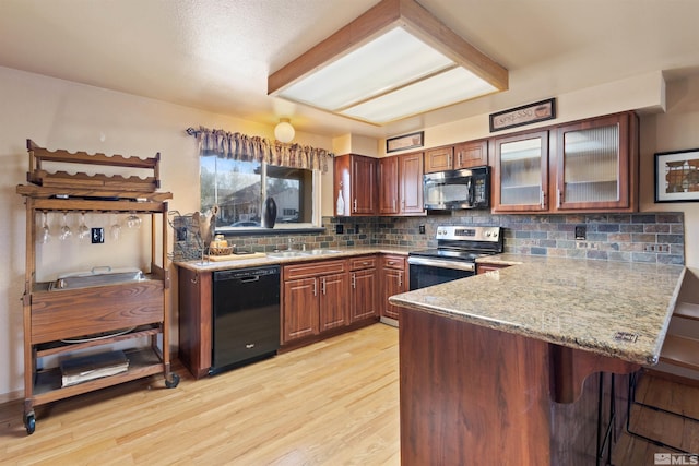 kitchen with black appliances, a peninsula, a breakfast bar, light wood finished floors, and a sink
