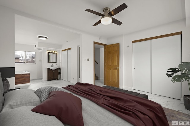bedroom featuring light marble finish flooring, two closets, a sink, and a ceiling fan