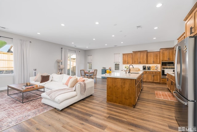 kitchen featuring stainless steel appliances, a sink, brown cabinetry, open floor plan, and a kitchen island with sink