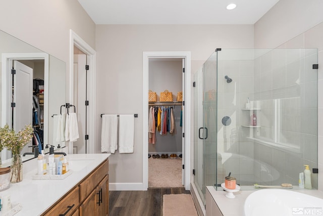 bathroom featuring wood finished floors, a stall shower, a walk in closet, and vanity