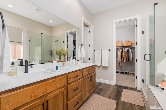 bathroom featuring wood finished floors, a shower stall, a spacious closet, double vanity, and baseboards