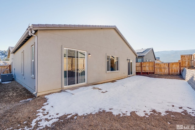 snow covered house featuring central AC unit, a fenced backyard, and stucco siding