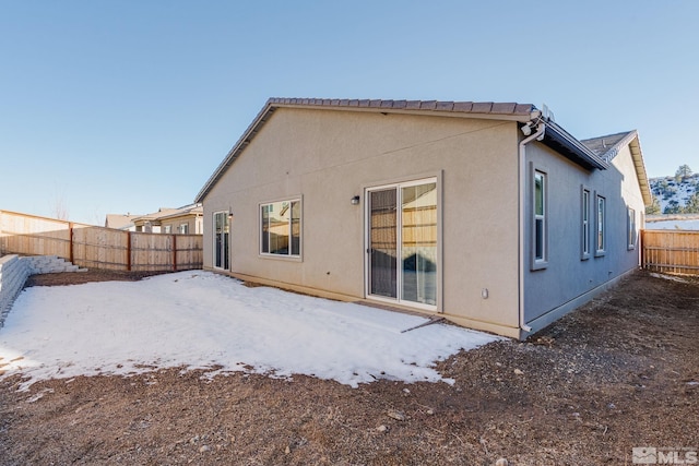 snow covered property featuring a fenced backyard and stucco siding