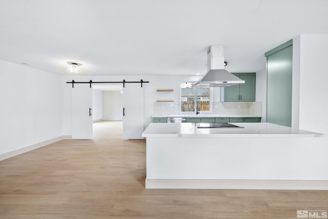 3575 Gull St, Reno, NV 89508 - kitchen featuring green cabinets, island exhaust hood, a barn door, backsplash, and light wood-type flooring