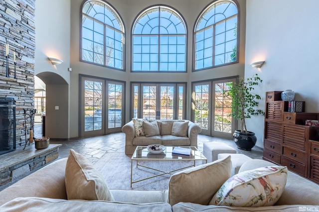 1185 Paddock Ln, Reno, NV 89521 - living room featuring healthy amount of natural light, a high ceiling, a stone fireplace, arched walkways, and french doors