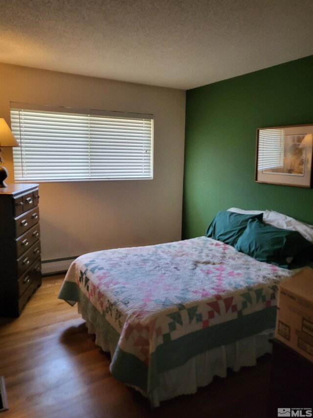 828 W Washington St, Carson City, NV 89703 - bedroom featuring light wood-style flooring, a textured ceiling, and a baseboard heating unit