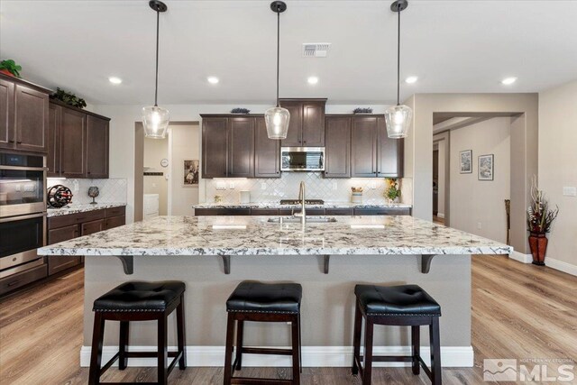 908 Sand Springs Dr, Sparks, NV 89441 - kitchen featuring appliances with stainless steel finishes, dark brown cabinetry, tasteful backsplash, a breakfast bar area, and light stone counters